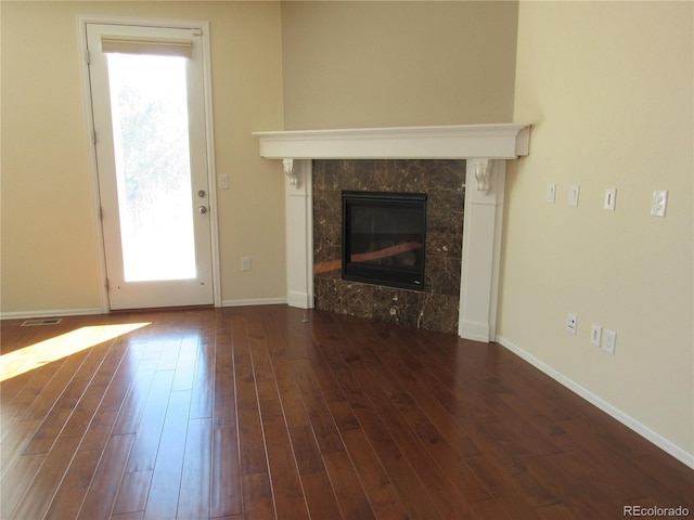 unfurnished living room featuring a fireplace, dark wood finished floors, visible vents, and baseboards