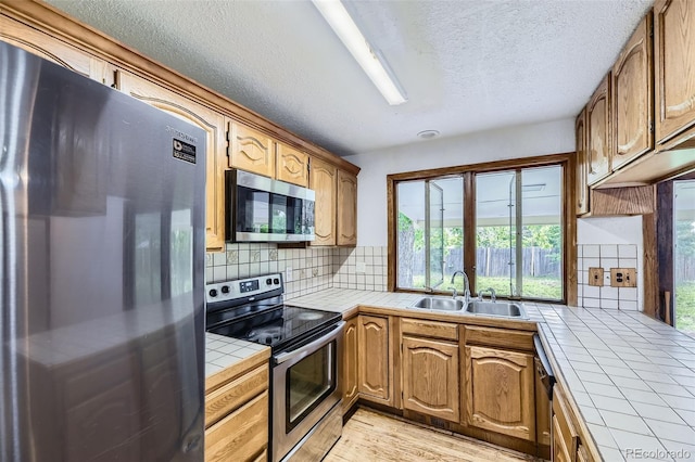 16293 E Brown Pl, Aurora, CO 80013 - kitchen featuring tile counters, appliances with stainless steel finishes, a sink, backsplash, and a textured ceiling