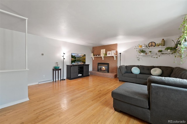 living room featuring baseboards, light wood-style flooring, and a brick fireplace