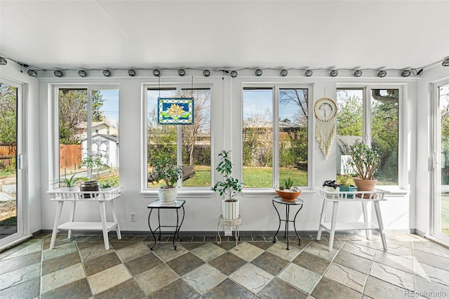 sunroom featuring rail lighting and stone tile flooring