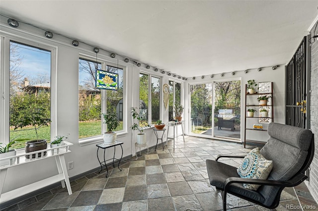 sunroom / solarium with rail lighting, baseboards, and stone tile floors