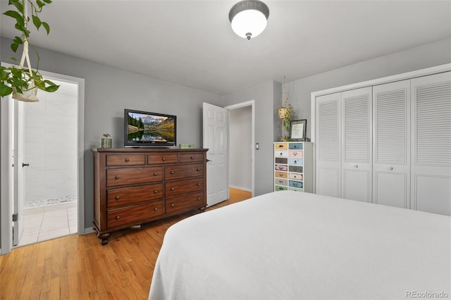 bedroom featuring baseboards, ensuite bath, light wood-type flooring, and a closet