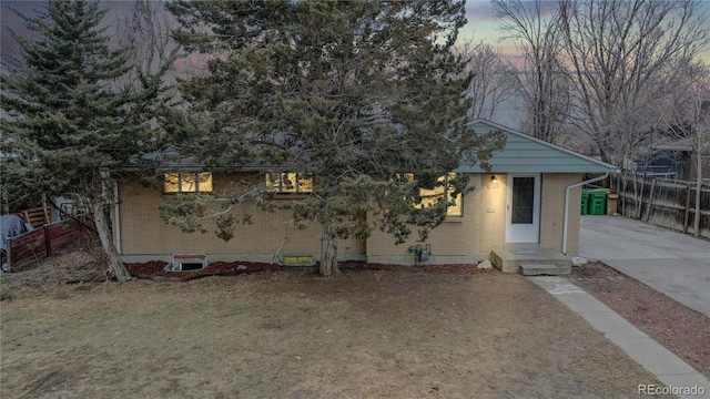 view of front of house featuring driveway, brick siding, and fence