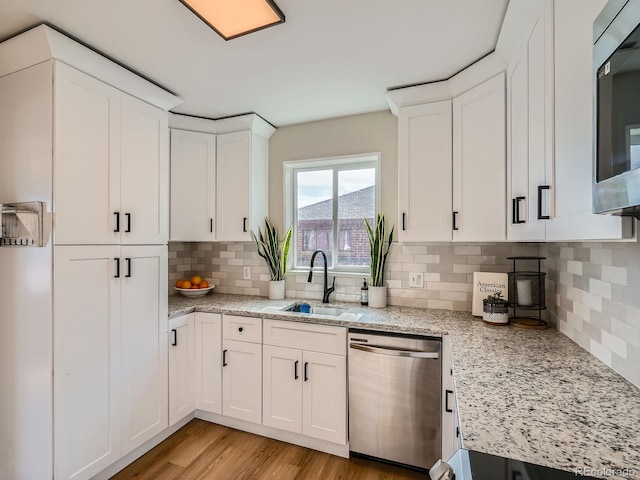 kitchen featuring stainless steel appliances, light stone counters, decorative backsplash, sink, and white cabinetry