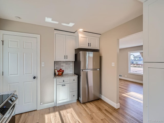 kitchen featuring appliances with stainless steel finishes, white cabinetry, light wood-type flooring, and decorative backsplash