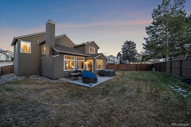 back house at dusk with a yard, a hot tub, and a patio