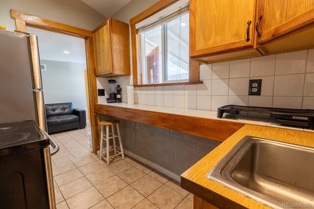 3021 Grape St, Denver, CO 80207 - kitchen with electric range, freestanding refrigerator, a sink, light tile patterned floors, and brown cabinets