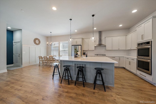 5663 W 96th Ave, Westminster, CO 80020 - kitchen featuring stainless steel appliances, wall chimney exhaust hood, a center island with sink, a kitchen bar, and light countertops