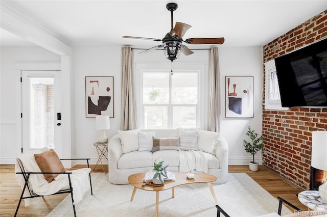 living area featuring light wood-style floors, baseboards, ceiling fan, and brick wall