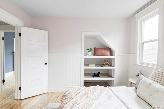 bedroom featuring multiple windows, light wood-style flooring, and a wainscoted wall