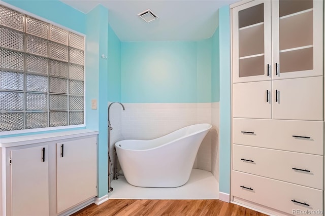 8095 E Lehigh Ave, Denver, CO 80237 - full bathroom featuring wood finished floors, a soaking tub, a wainscoted wall, and tile walls