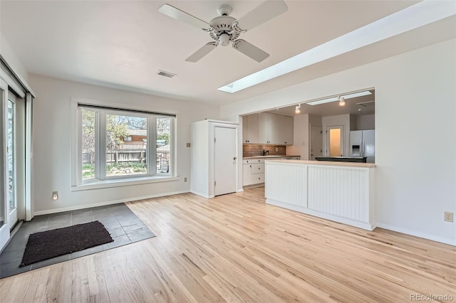 8095 E Lehigh Ave, Denver, CO 80237 - unfurnished living room with light wood-style flooring, rail lighting, a ceiling fan, baseboards, and a skylight