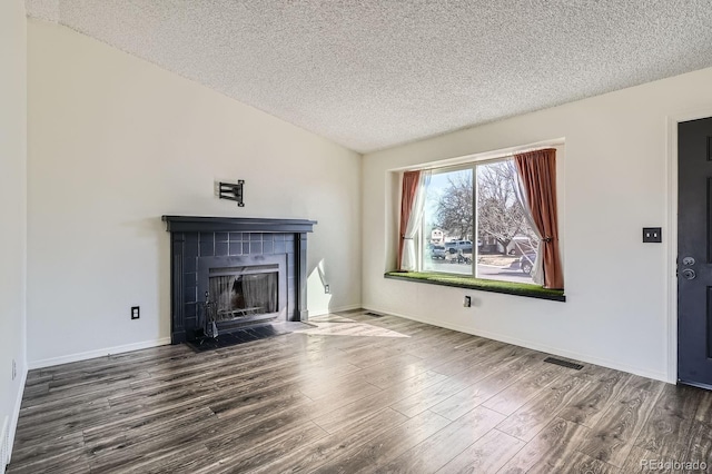 unfurnished living room featuring baseboards, lofted ceiling, a tile fireplace, wood finished floors, and a textured ceiling