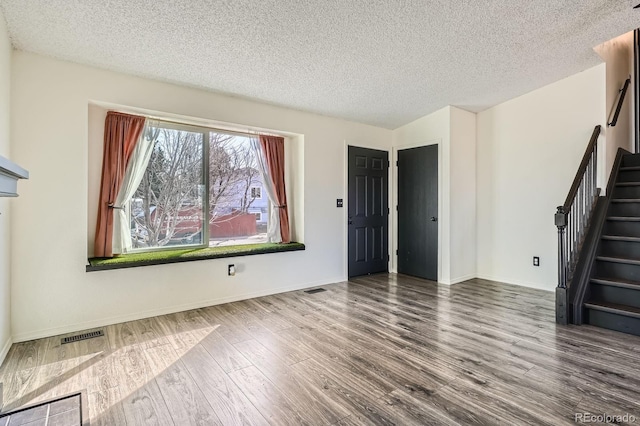 unfurnished living room with stairway, a textured ceiling, visible vents, and wood finished floors