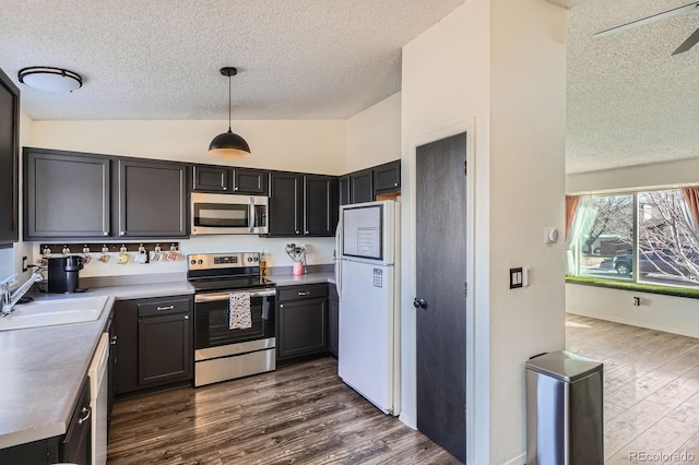 kitchen with a sink, a textured ceiling, dark wood finished floors, appliances with stainless steel finishes, and vaulted ceiling