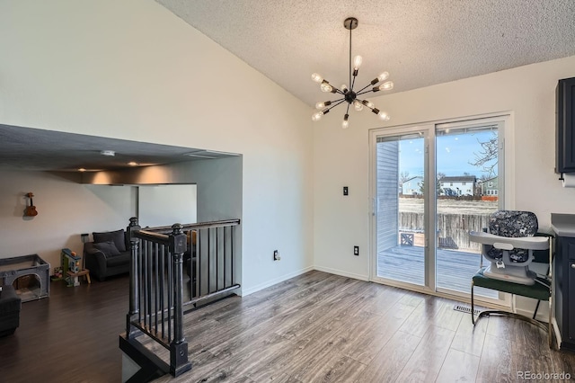 interior space featuring a notable chandelier, lofted ceiling, a textured ceiling, wood finished floors, and baseboards