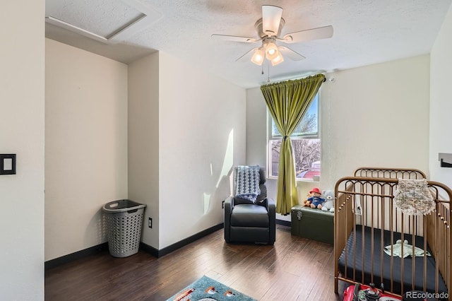 bedroom featuring a crib, a textured ceiling, wood finished floors, baseboards, and attic access