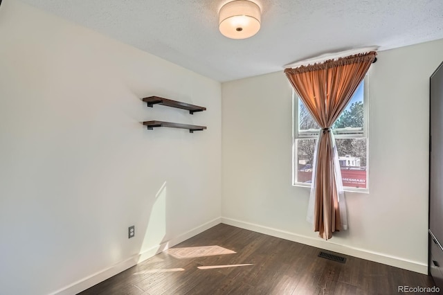 spare room with dark wood-style floors, a textured ceiling, and baseboards