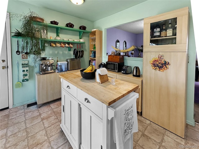 kitchen featuring stone finish floor, wooden counters, open shelves, white cabinets, and stainless steel microwave
