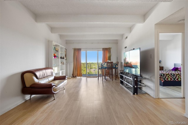 sitting room featuring a textured ceiling, light hardwood / wood-style flooring, and beamed ceiling