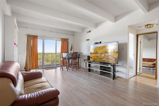 living room featuring a textured ceiling, light wood-type flooring, and beam ceiling