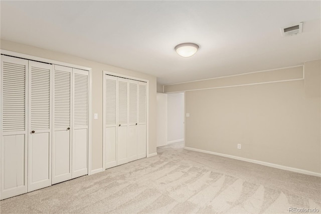 unfurnished bedroom featuring carpet floors, baseboards, multiple closets, and visible vents