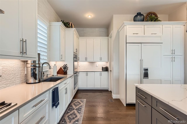 10119 Bellwether Ln, Lone Tree, CO 80124 - kitchen featuring light stone countertops, a sink, dark wood finished floors, white cabinetry, and tasteful backsplash