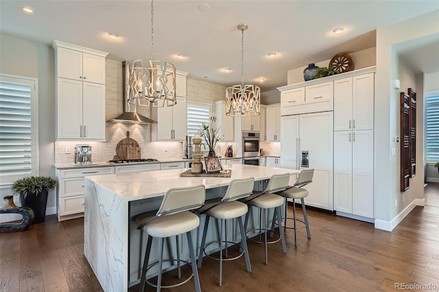 10119 Bellwether Ln, Lone Tree, CO 80124 - kitchen with wall chimney range hood, appliances with stainless steel finishes, an inviting chandelier, white cabinetry, and dark wood-type flooring