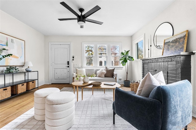 living area with wood finished floors, ceiling fan, baseboards, and a brick fireplace