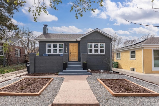 bungalow-style home featuring brick siding, a vegetable garden, and a chimney