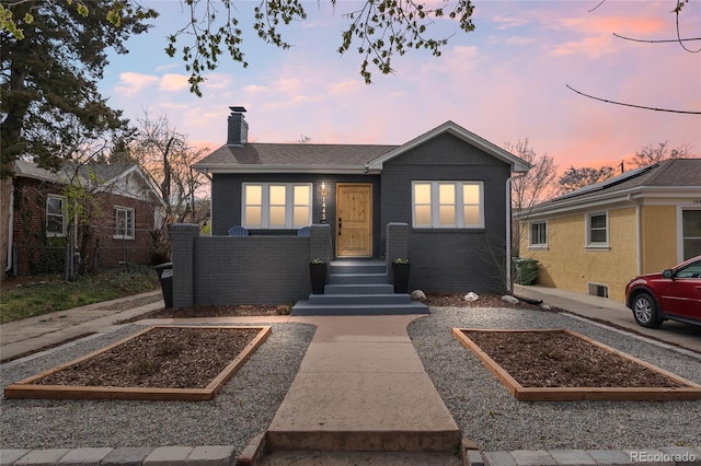 bungalow-style house with a garden, a chimney, fence, and brick siding