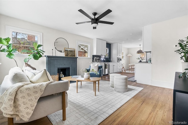 living area featuring light wood finished floors, a ceiling fan, a fireplace, and a healthy amount of sunlight