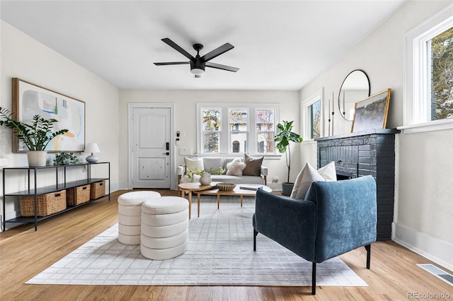 living room with light wood-style floors, a fireplace, a ceiling fan, visible vents, and baseboards