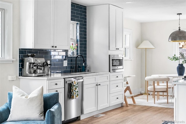 kitchen featuring tasteful backsplash, white cabinetry, light wood-style floors, stainless steel appliances, and a sink