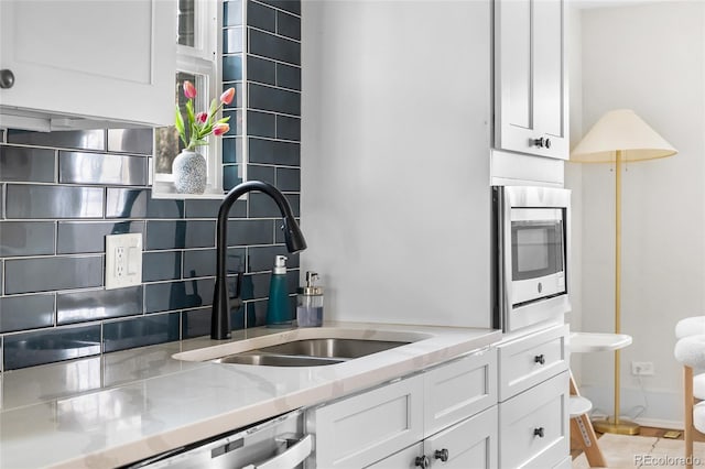 kitchen with tasteful backsplash, white cabinetry, light stone countertops, appliances with stainless steel finishes, and a sink