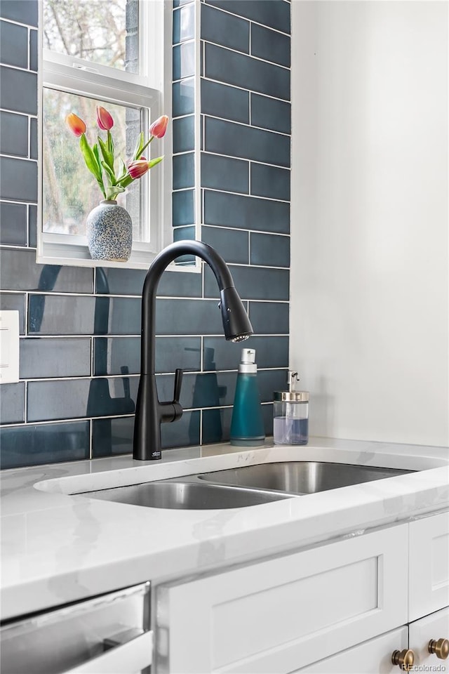 details featuring decorative backsplash, a sink, white cabinetry, and dishwashing machine