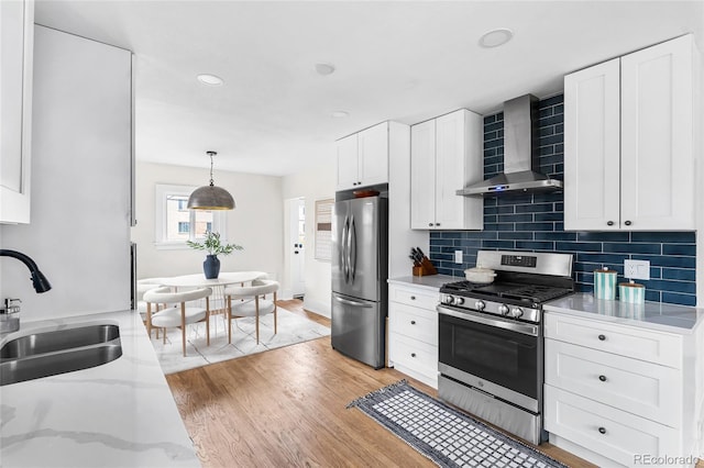 kitchen featuring light wood-style flooring, wall chimney range hood, white cabinets, a sink, and stainless steel appliances