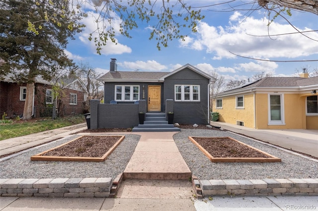 bungalow-style home featuring a chimney, a vegetable garden, and brick siding