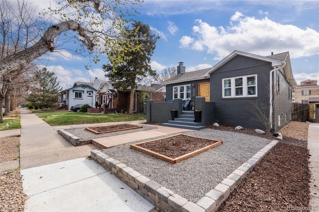 bungalow-style house featuring fence, brick siding, a chimney, and a garden