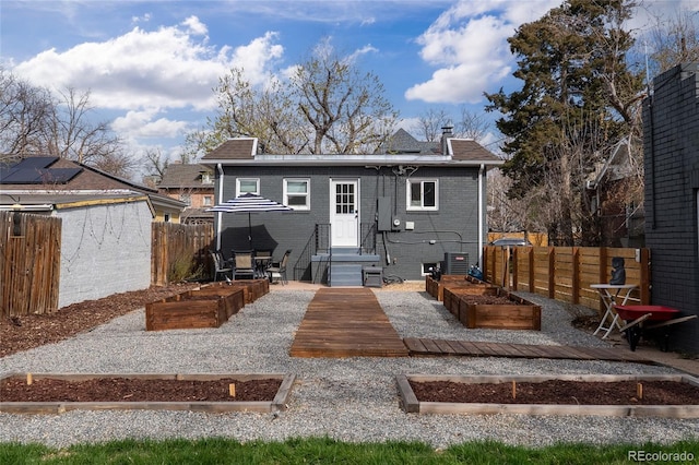 rear view of property with brick siding, fence, and a vegetable garden