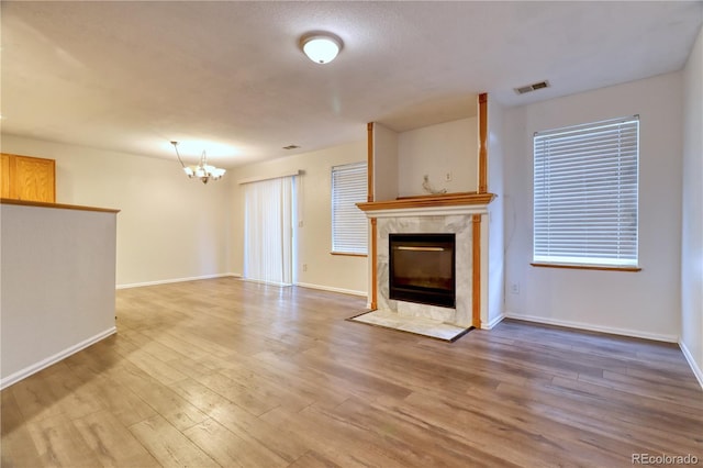 unfurnished living room with a fireplace, an inviting chandelier, and light hardwood / wood-style floors