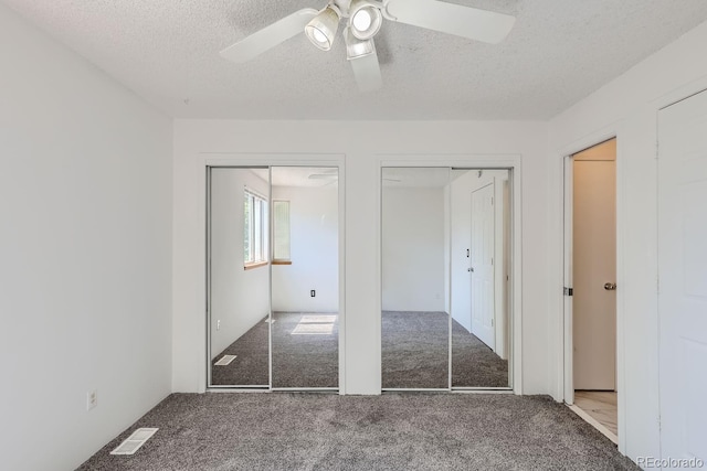 unfurnished bedroom featuring visible vents, multiple closets, carpet flooring, a textured ceiling, and a ceiling fan