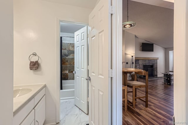 full bath with marble finish floor, a fireplace with raised hearth, bathing tub / shower combination, vanity, and vaulted ceiling