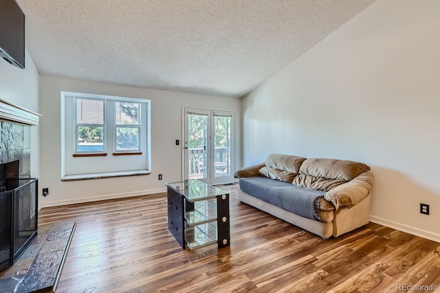 living area featuring wood finished floors, baseboards, a high end fireplace, vaulted ceiling, and a textured ceiling