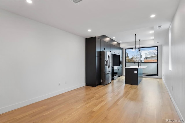 kitchen featuring light wood-style flooring, visible vents, hanging light fixtures, stainless steel refrigerator with ice dispenser, and an island with sink