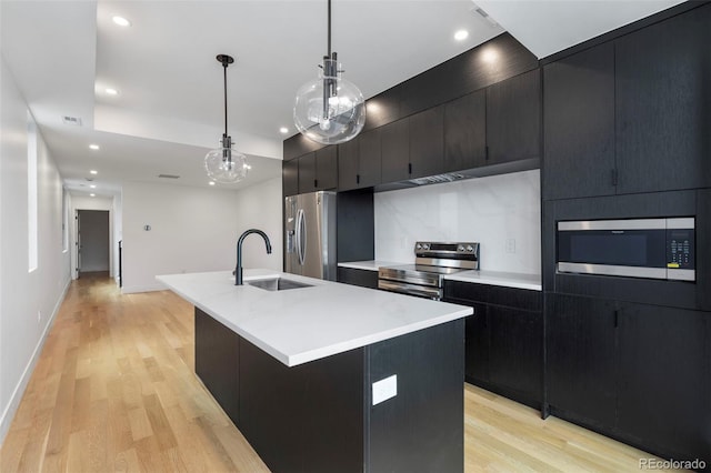 kitchen featuring an island with sink, appliances with stainless steel finishes, dark cabinets, light countertops, and a sink