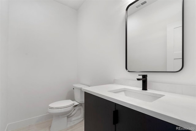 bathroom with baseboards, visible vents, toilet, wood finished floors, and vanity