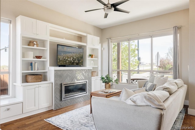 living area featuring a ceiling fan, dark wood finished floors, built in features, and a tile fireplace