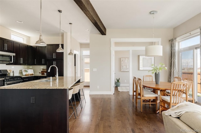 kitchen with light stone countertops, a kitchen breakfast bar, dark wood-type flooring, a sink, and stainless steel appliances