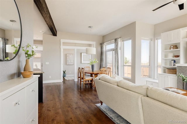 living area with beamed ceiling, a ceiling fan, baseboards, and dark wood finished floors